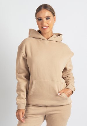Bež jopa s kapuco iz mehkega materiala, z žepom na sprednji strani, sproščenim krojem in rebrastimi manšetami. Preprost, minimalističen dizajn.