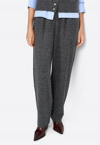 Pantalons à motif pied-de-coq gris avec une coupe ample, dotés de plis et d'une finition texturée. Associés à des chaussures à talons aiguilles bordeaux.