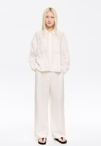 Linen shirt with a button-up design, featuring two front pockets and a textured pattern, paired with loose, wide-leg linen pants in white.