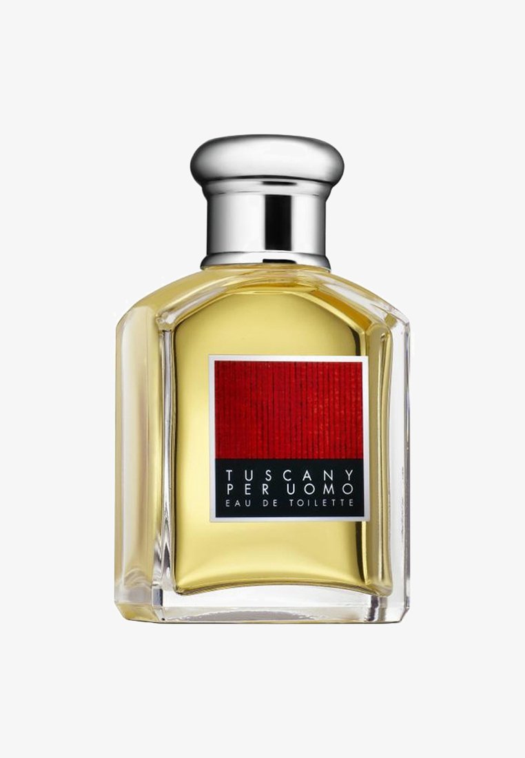 Klar glasflaska med en bred silverkork; gul vätska inuti; etikett med en röd ruta och svart text som säger "Tuscany Per Uomo Eau de Toilette."