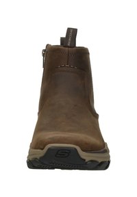 Stivale alla caviglia Skechers in pelle marrone con linguetta e suola in gomma, visto frontalmente su sfondo bianco.