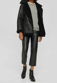 Schwarze Lederjacke mit Lammfellkragen, grau gestreifter Pullover, schwarze Leder-Cropped-Hosen und schwarze Stiefeletten.