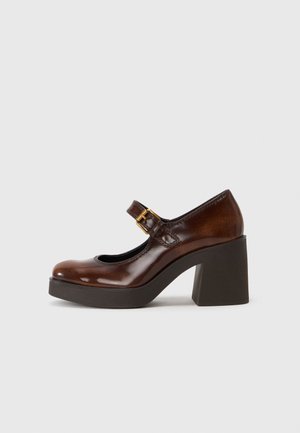 Zapato Mary Jane de charol marrón con tacón cuadrado, tira ajustable con hebilla y diseño de punta redonda. Textura suave y acabado brillante.