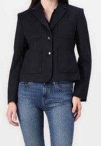 Granatowa marynarka o dopasowanym kroju, z dwiema przednimi kieszeniami, guzikami w kolorze srebrnym i klapami w stylu notched. Noszona z dopasowanymi niebieskimi dżinsami.