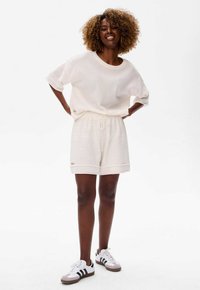 Loungewear set in crèmekleur, met een losse, korte mouwen top en bijpassende shorts met trekkoord, gemaakt van een gestructureerde stof.