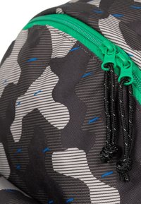 Zaino nero con motivo a camouflage grigio, dotato di zip verdi e lacci neri. Tessuto testurizzato con piccoli accenti blu.