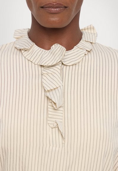 Cream blouse with thin vertical stripes, features a ruffled collar and a central ruffle detail. Soft texture, button closure at the neck.