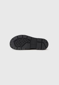 Suola di scarpa in gomma nera con un motivo di grip testurizzato, caratterizzato da profonde scanalature e creste per una maggiore trazione. Design piatto e ampio con una costruzione robusta.