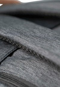 Schwarzer Stoff mit glatter Textur und sichtbaren Nähten, die geschichtete Abschnitte zeigen und einen Blick auf einen Reißverschluss ermöglichen. Nahaufnahme des Materials.