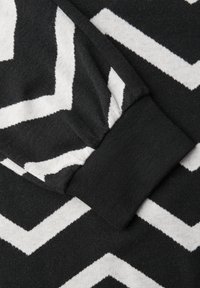 Szczegół czarno-białego swetra z wzorem w zygzak. Tkanina jest miękka, z prążkowanym mankietem i gładką fakturą.