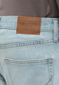 Ανοιχτό μπλε τζιν παντελόνι με δερμάτινη ετικέτα που γράφει "HOLLISTER" στη ζώνη και διακοσμητική ραφή στις πίσω τσέπες.