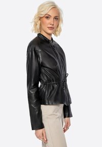 Giacca in pelle nera con colletto alto, vita stretta e maniche lunghe. Tessuto liscio, design minimalista, con chiusura frontale a zip.
