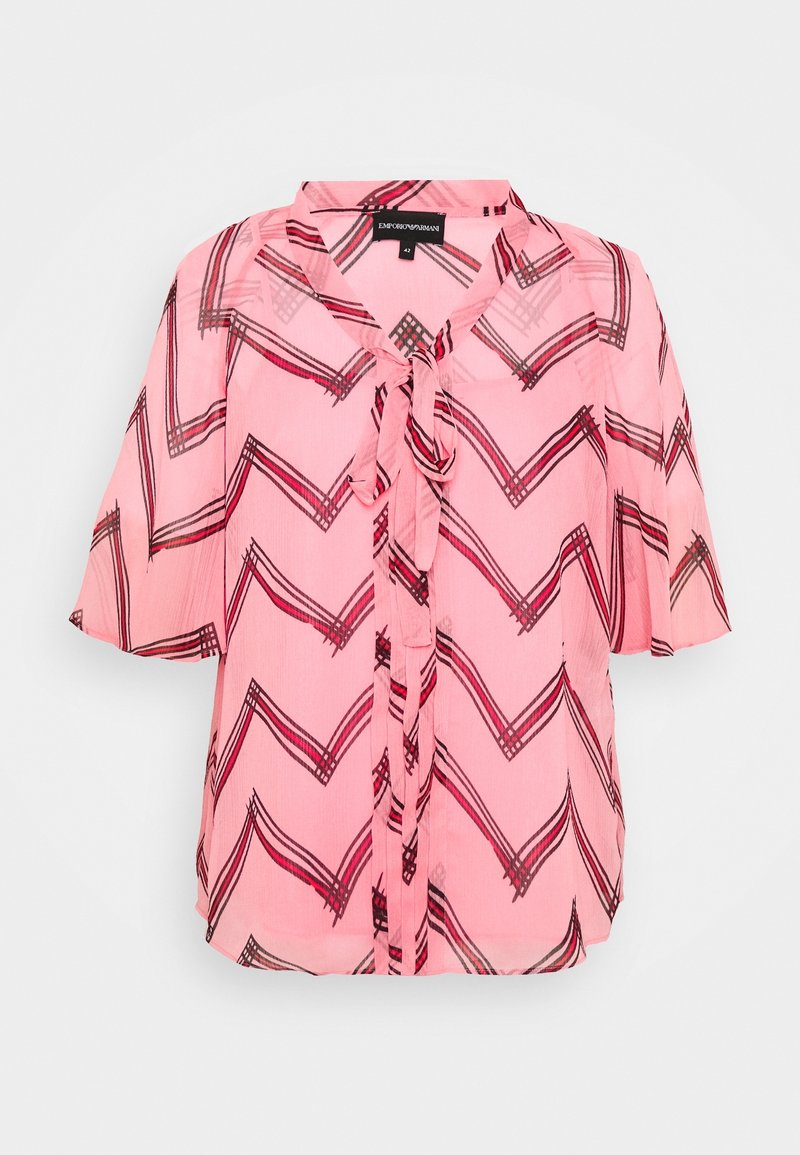 Blusa rosa trasparente con motivo a zigzag in nero e rosso scuro. Presenta una chiusura con nodo sul davanti e maniche corte. Tessuto leggero.
