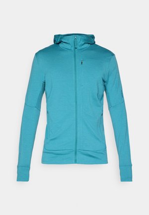 Fleece azul-petróleo com fecho éclair, mangas longas, buracos para os polegares e punhos ajustados, exibida contra um fundo claro e liso.