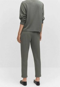 Sweatshirt court à manches longues vert olive associé à un pantalon de survêtement fuselé. Texture lisse, manches retroussées et design simple. Chaussures noires à enfiler.