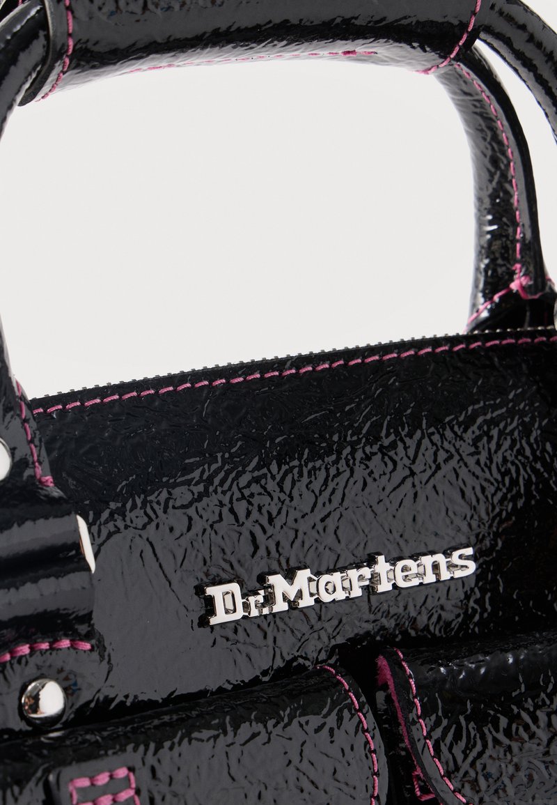 Glanzende zwarte Dr. Martens handtas met roze stiksels en zilverkleurig metalen logodetail op een gestructureerd oppervlak.