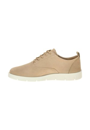 Beige leren casual veterschoen met witte rubberen zool en trekriempje bij de hiel, vanaf de zijkant getoond op een witte achtergrond.