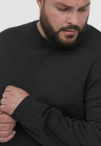 Pull en maille noir à col rond. Présente des poignets et un ourlet côtelés. Le matériau semble doux et durable, avec une coupe ajustée.