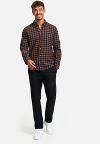 Brun og marineblå ternet skjorte med knaplukning, lavet af bomuldsmateriale, med lange ærmer, parret med sorte bukser og hvide sneakers.