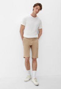 Lichte beige shorts en een aansluitend wit T-shirt. De shorts hebben een casual snit, en de man draagt witte sneakers en sokken tot aan de enkel.
