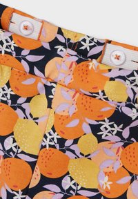Der Baumwollstoff hat einen dunklen Hintergrund mit orangefarbenen und gelben Obstmustern, akzentuiert durch lila Blätter und weiße Knöpfe mit orangefarbener Nähte.