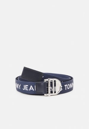 Navyblauwe stoffen riem met witte "Tommy Jeans" tekst en zilveren D-ringgesp met zwarte leren accenten, opgerold op een witte achtergrond.