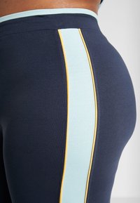 Námořnické sportovní legíny s mátově zeleným a žlutým bočním pruhem, vyrobené z elastického materiálu s hladkou strukturou.