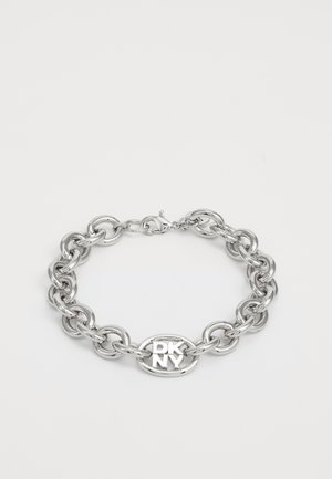 Silver metal chain bracelet with large links, featuring an oval charm engraved with "DKNY." Smooth texture and secure clasp.
