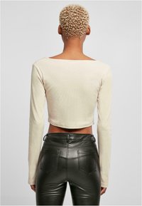 Krém színű, hosszú ujjú crop top, négyzet alakú dekoltázzsal, amelyet magas derekú fekete műbőrnadrággal párosítanak, hátul zsebekkel.