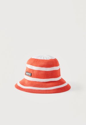 Oransje og hvitstripet strikket bøttehatt med en liten svart og hvit logopatch på siden, på en ensfarget lys bakgrunn.