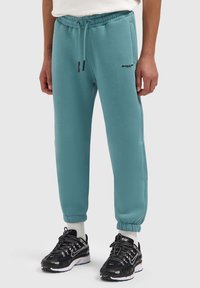 Turquoise joggers met een elastische taille en manchetten. Voorzien van een trekkoord en een zwart logo op de linker bovenbeen. Zachte, gestructureerde stof.