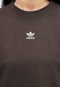 Καφέ φούτερ με στρογγυλή λαιμόκοψη και ριμπ μανσέτες. Διαθέτει λευκό κεντημένο λογότυπο Adidas στο στήθος. Μαλακή υφή.
