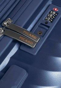 Maleta rígida azul con superficie texturizada, que presenta cremalleras metálicas con el logotipo grabado "PICARD" y un mecanismo de bloqueo aprobado por la TSA.