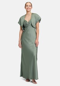 Satin groene avonddress met een aansluitende corsage, geraffineerde details en korte gedrapeerde mouwen. De jurk valt tot op de vloer met een lichte glans.