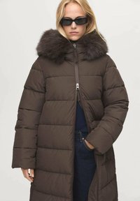 Abrigo tipo puffer marrón con cuello de pelaje sintético, con cierre de cremallera en el frente y diseño acolchado, y mangas largas, adecuado para el clima frío.