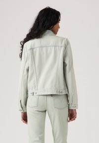 Φωτεινό πράσινο τζιν μπουφάν με κουμπωτά μανίκια, δύο πίσω τσέπες και λεπτομέρεια τσέπης με καπάκι. Ομαλή υφή με ορατές ραφές.