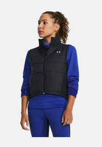 Gilet imbottito nero con colletto alto e zip frontale. Indossato sopra una maglietta a maniche lunghe blu, che mostra un design trapuntato leggero.
