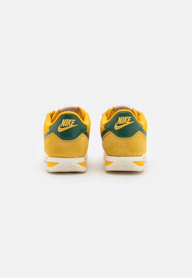 Zapatillas Nike con ante amarillo y detalles en cuero verde. Suela intermedia blanca con detalle naranja. Presenta el logo en el talón y en la lengua.