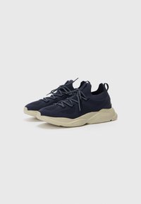 Marineblå mesh joggesko med en beige såle, som har teksturert overdel, kontrasterende snøringer og et lavt snitt for enkel påkledning.