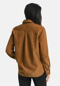 Brown corduroy shirt with a back yoke detail, button-down collar, and long sleeves, displayed from the back. Smooth texture and subtle sheen.