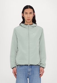 Lys mintgrøn zip-up jakke lavet af letvægtsmateriale med hætte, der har et frontlogo, elastiske ærmer og to sidelommer.