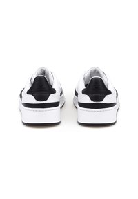 Un paio di sneakers bianche con dettagli neri sulla parte posteriore e sulla suola intermedia, viste da dietro su uno sfondo bianco.