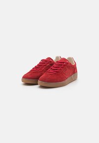 Red suede sneakers with matching laces, rounded toe, and tan rubber sole. Features subtle stitching details for added texture.