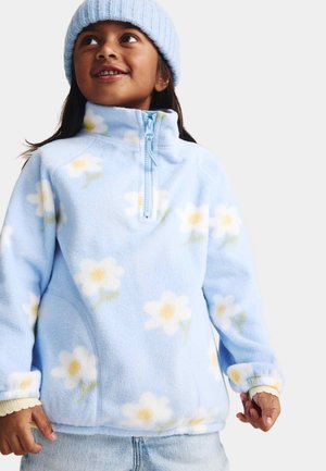 Forro polar azul claro con estampado floral que presenta flores blancas y amarillas. Tiene un cuello de media cremallera y puños blancos acanalados.