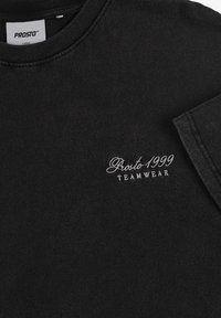 Czarna bawełniana koszulka z okrągłym dekoltem i krótkimi rękawami. Z przodu po lewej stronie subtelne białe hafty z napisem "Prosto 1999 TEAMWEAR."