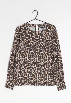 Blouse à manches longues avec motif léopard suspendue à un cintre noir sur fond blanc.
