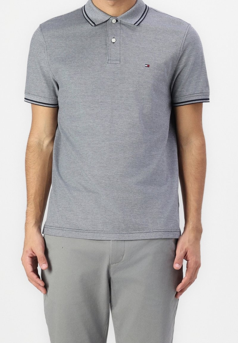 Polo gris en mélange de coton, avec un col et des poignets rayés contrastants, une patte à deux boutons et un petit logo sur la poitrine.