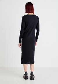 Long, form-fitting, black knit dress with long sleeves and side slits, featuring a ribbed texture and soft fabric.