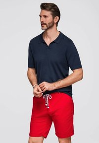 Mörkblå pikétröja med korta ärmar, matchad med röda shorts med dragsko och uppvikt hem. Enkelt design med en mjuk textur.