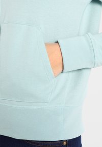 Sweat-shirt bleu clair avec poche kangourou et poignets côtelés. Texture douce en mélange de coton, avec des détails surpiqués le long de l'ourlet.